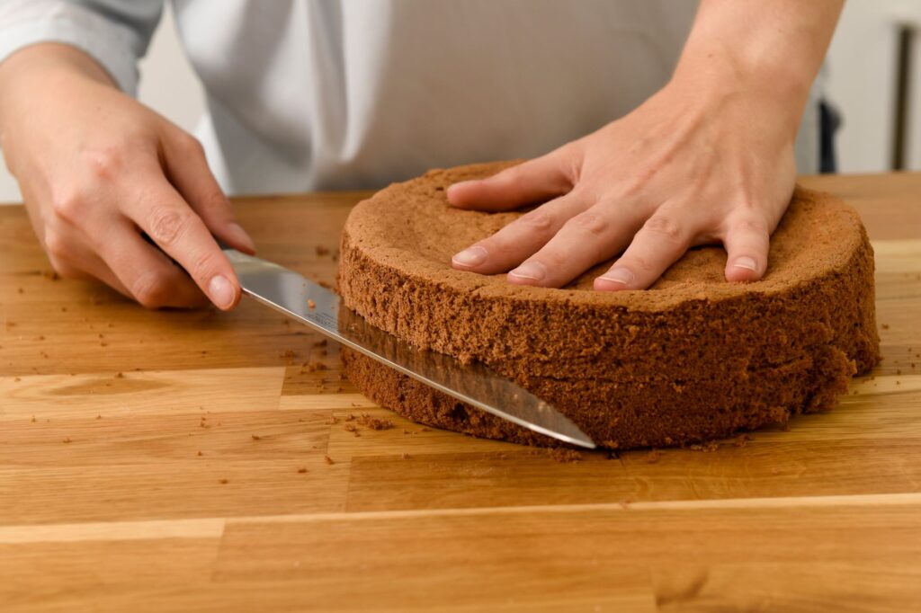 Gros plan sur une personne tranchant un gâteau au chocolat fait maison fraîchement cuit sur une table de cuisine en bois.