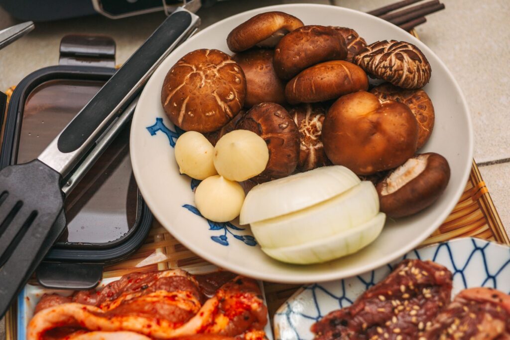 Une assiette de champignons frais et d'oignons prêts à être grillés au barbecue, accompagnés de viande marinée crue.