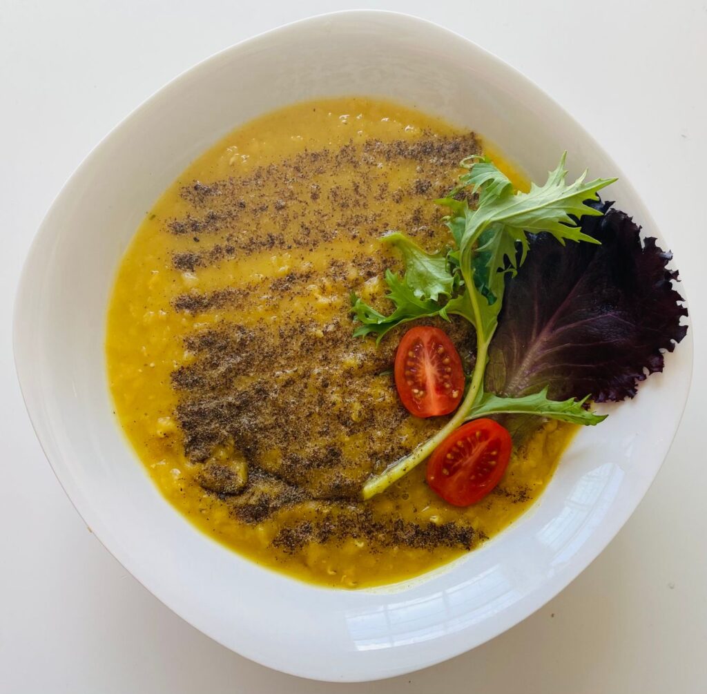 Gros plan sur une soupe de lentilles crémeuse garnie de légumes verts et de tomates dans un bol blanc.